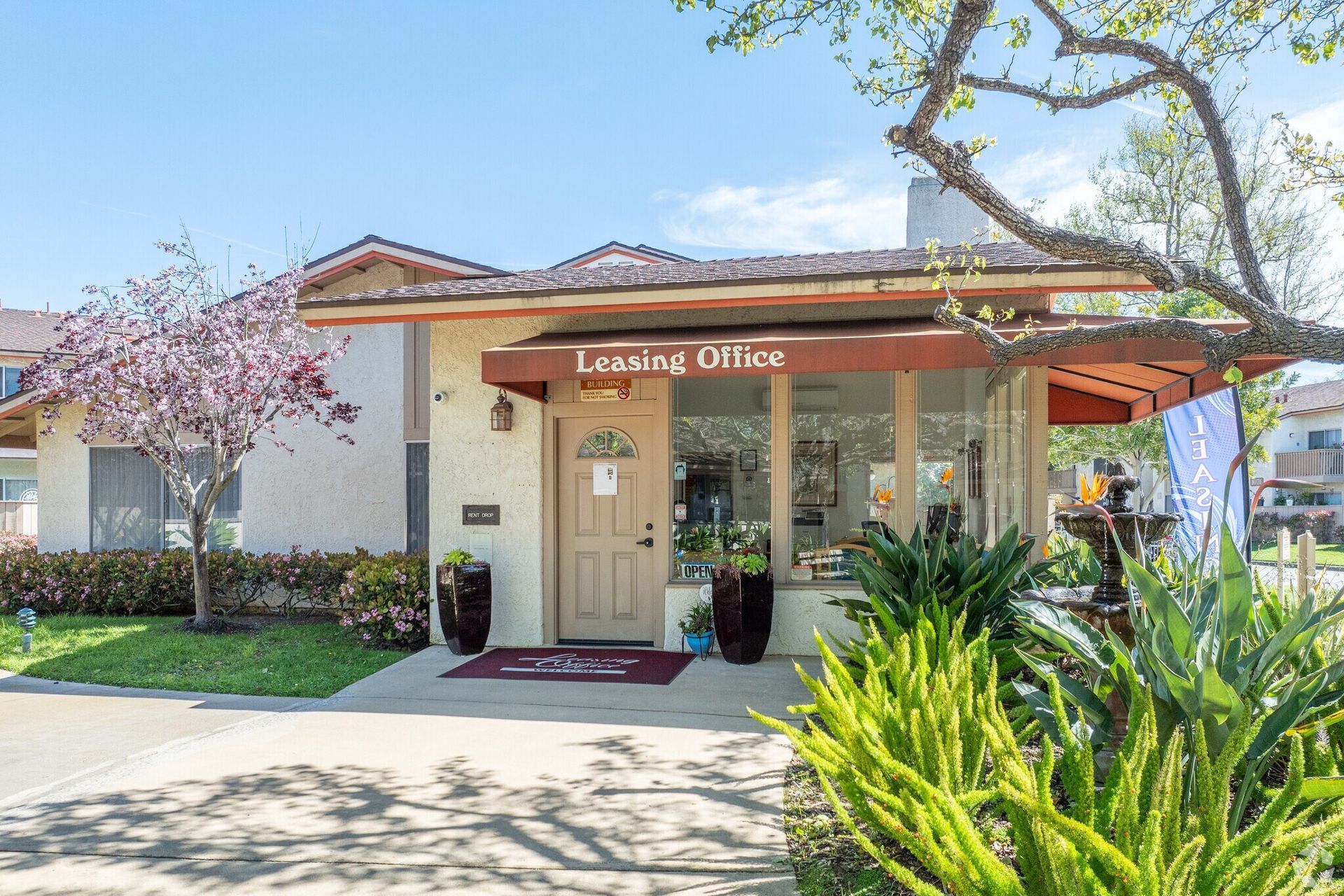 Living Office storefront with tan exterior, red awning, and desert landscaping on a sunny day