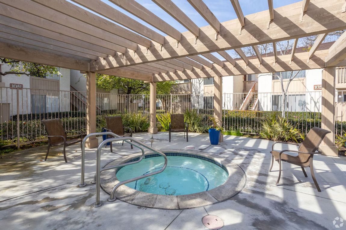 Courtyard hot tub under a wooden pergola with lounge chairs and apartment buildings nearby