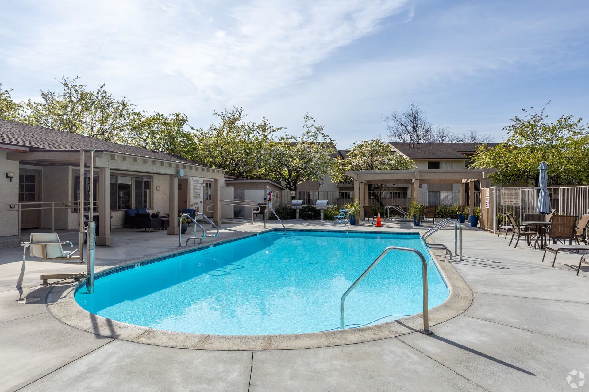 Outdoor swimming pool with blue water, lounge chairs, and cabanas in a sunny courtyard