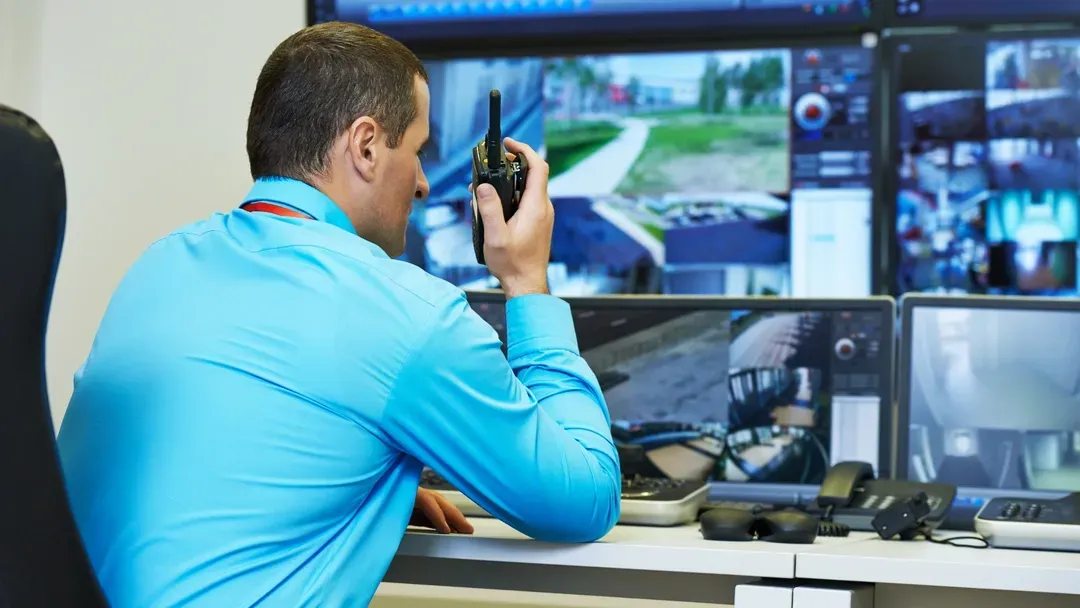 Un homme en chemise bleue est assis à un bureau et parle dans un talkie-walkie.