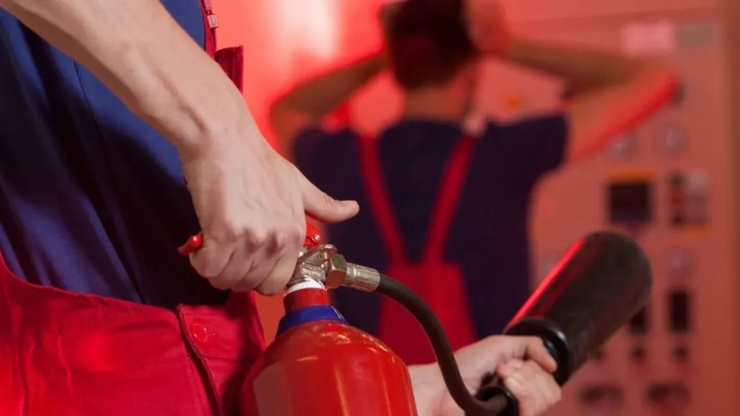 Un homme tient un extincteur devant un feu rouge.