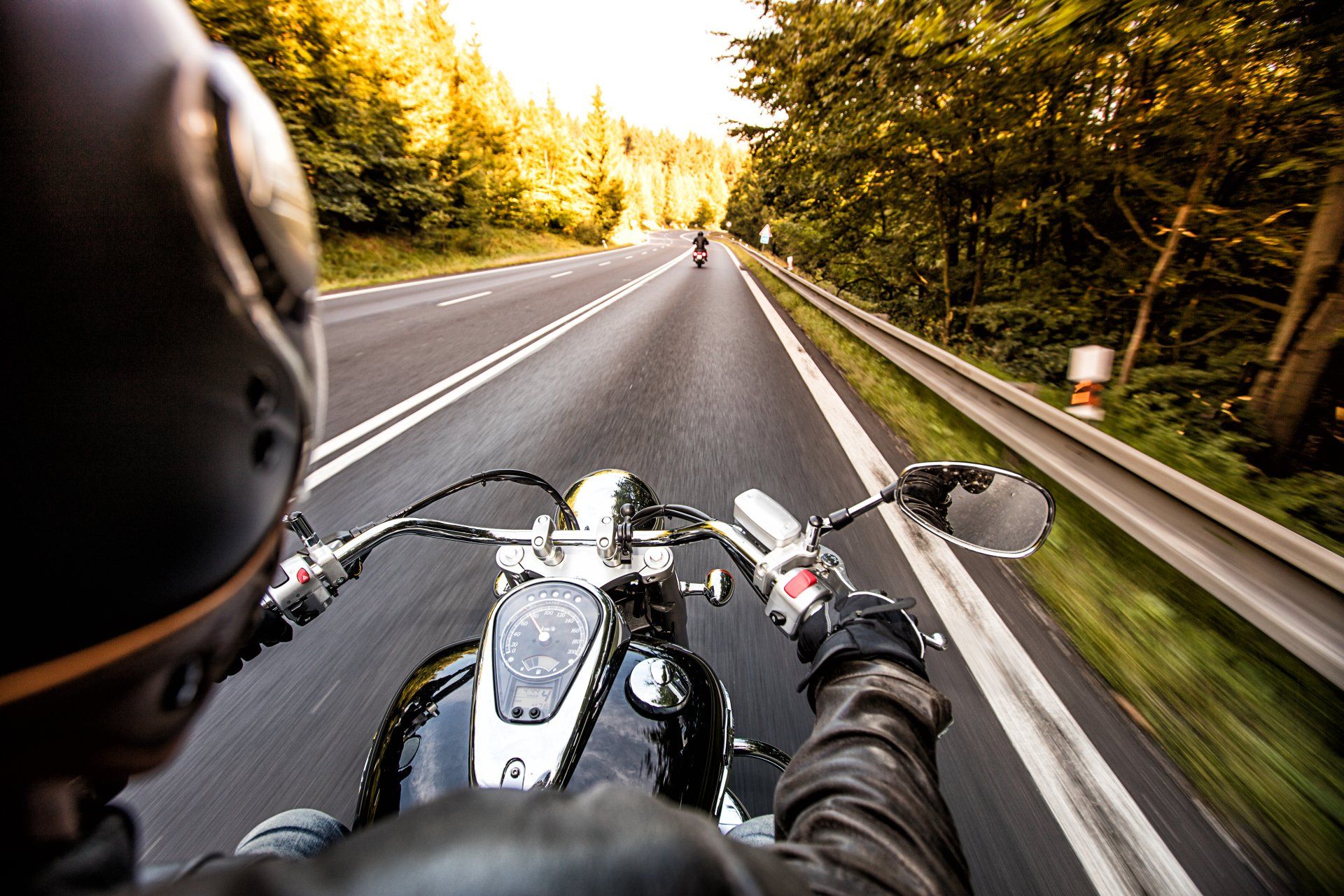 Un motocycliste circule sur une route pavée à travers une forêt.