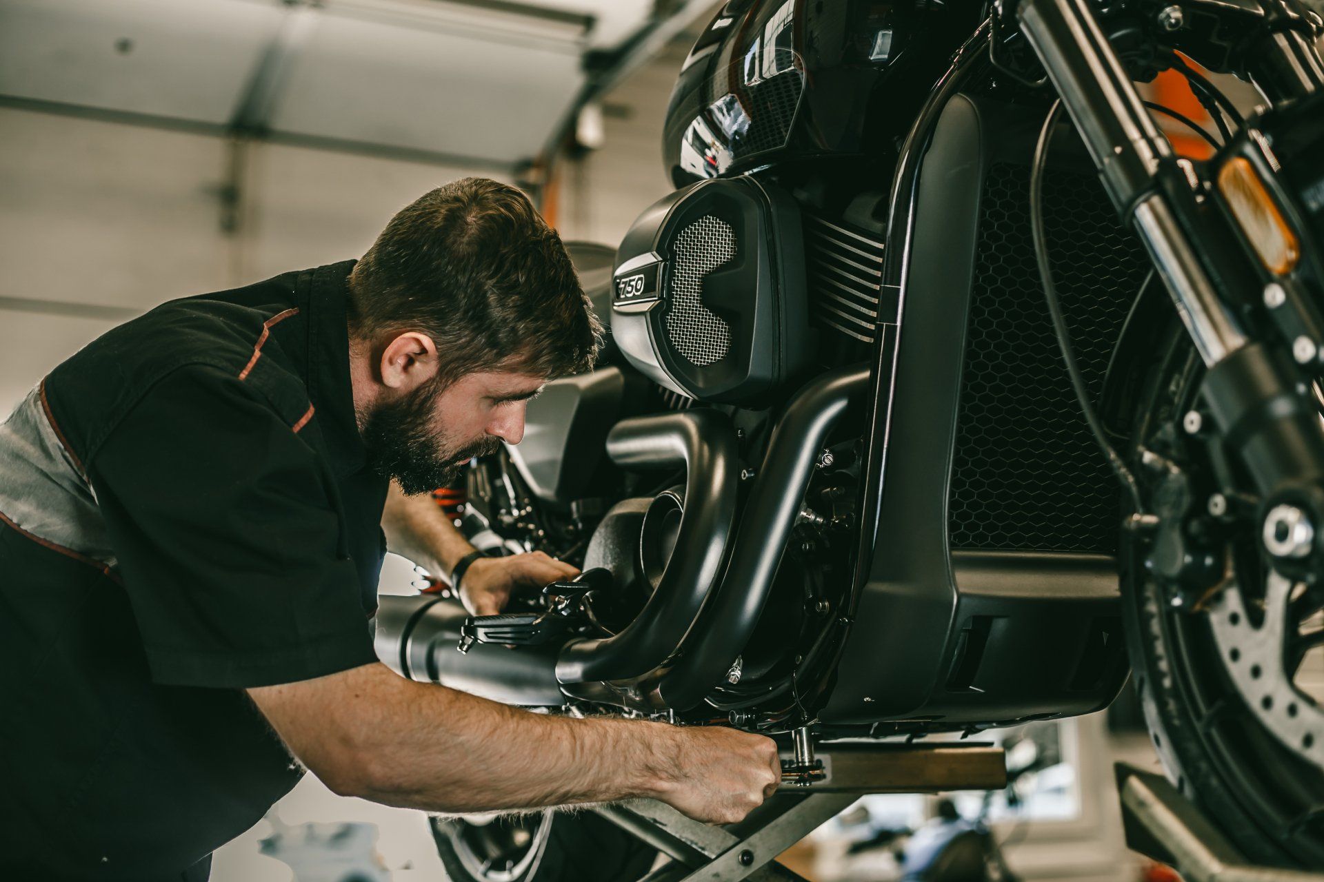 Mécanicien travaillant sur une moto noire dans un garage.
