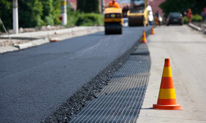 Road paving in progress, with a steamroller and orange traffic cone on the side. Road paving in progress, with a steamroller and orange traffic cone on the side.