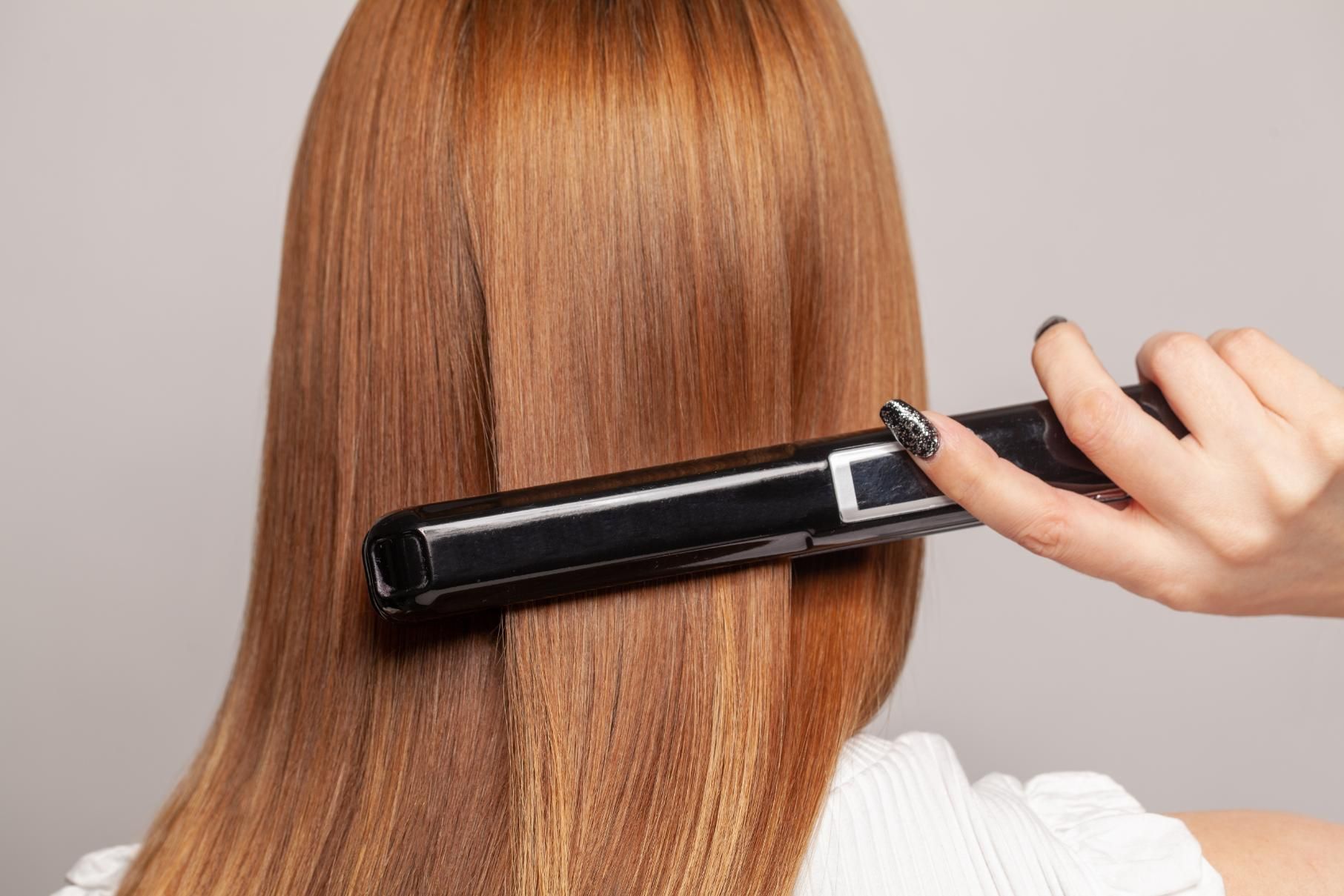 A Woman is Getting Her Hair Straightened With a Flat Iron — Elysian Salon In Wyong, NSW
