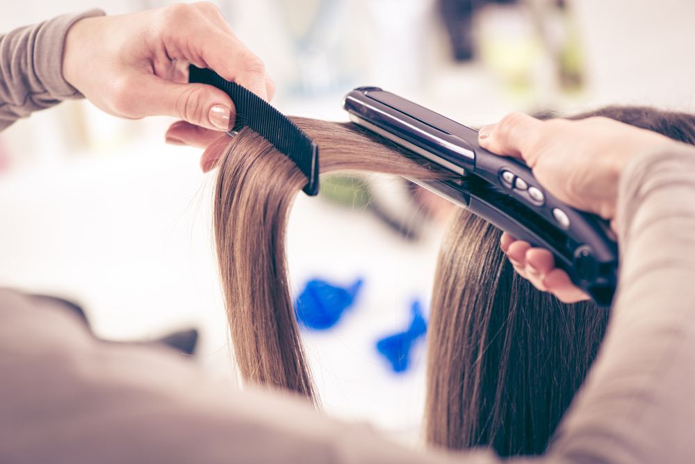 A Woman is Getting Her Hair Straightened by a Hairdresser — Elysian Salon In Wyong, NSW