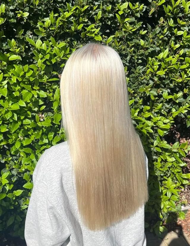 A Woman With Long Blonde Hair is Standing in Front of a Bush — Choo Choo Hair and Beauty In Wyong, NSW A Woman With Long Blonde Hair is Standing in Front of a Bush — Elysian Salon In Wyong, NSW
