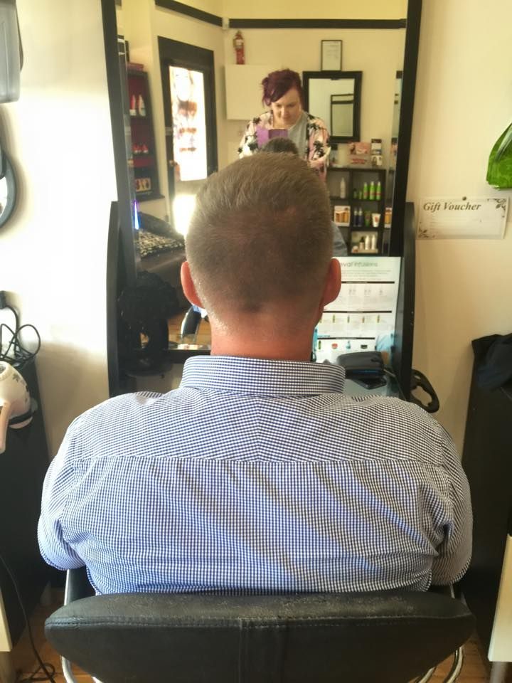 A Man in a Blue Shirt is Sitting in a Chair in Front of a Mirror — Elysian Salon In Wyong, NSW