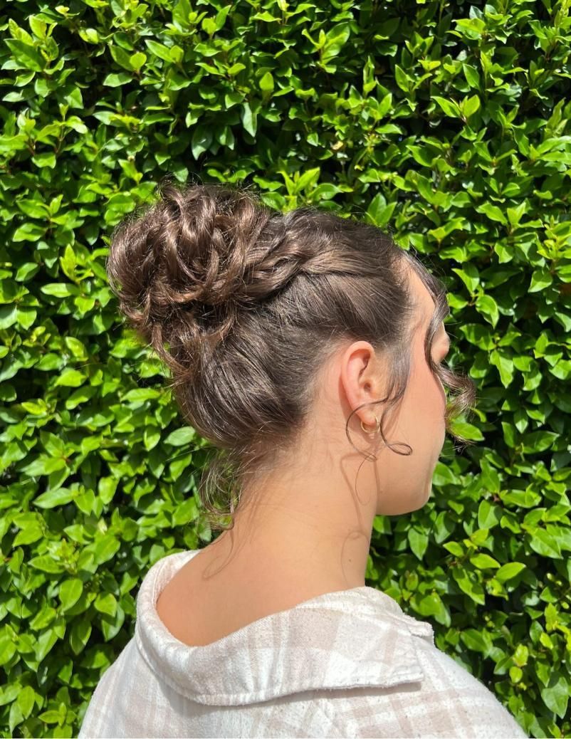 A Woman With Her Hair in a Bun is Standing in Front of a Bush — Elysian Salon In Wyong, NSW