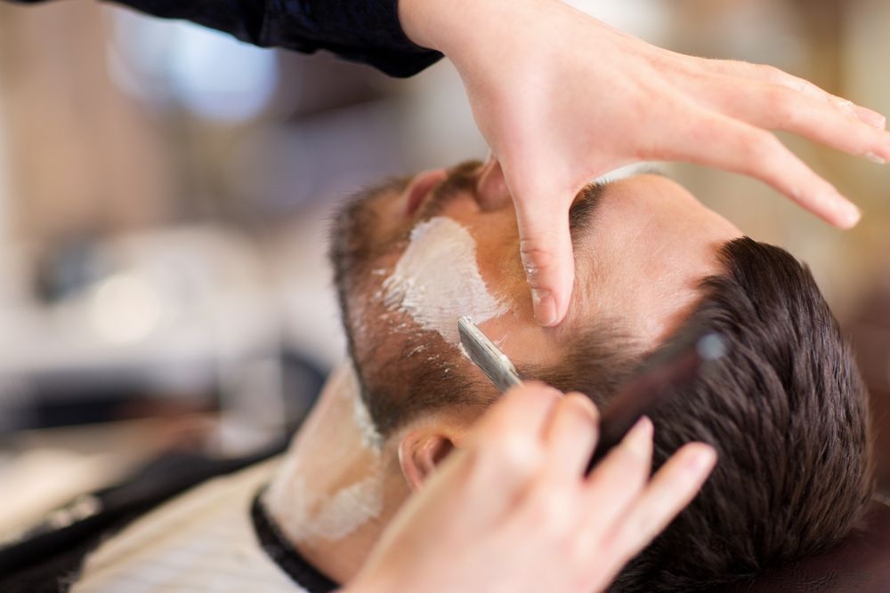 A Man is Getting His Beard Shaved by a Barber in a Barber Shop — Elysian Salon In Wyong, NSW