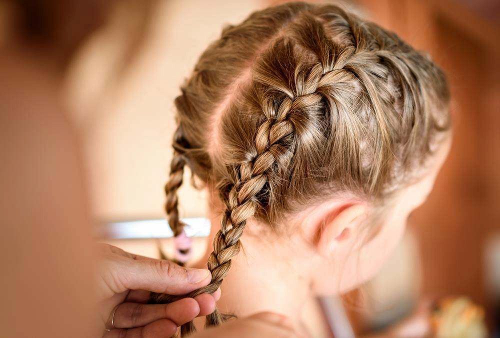 A Braided Hairstyle Being Finished by Hands in a Warmly Lit Room — Elysian Salon In Wyong, NSW