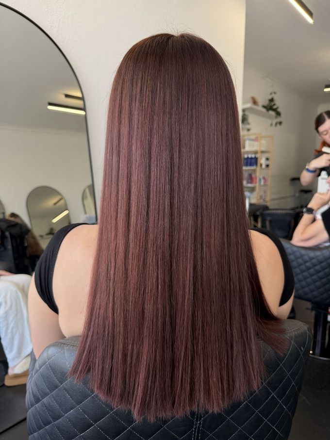Hairdresser Applying Dye to Brown Hair With Gloved Hands and a Brush — Elysian Salon In Wyong, NSWv Straight Dark Brown Hair Down the Back in a Salon Chair, With a Mirror and Stylist — Elysian Salon In Wyong, NSW