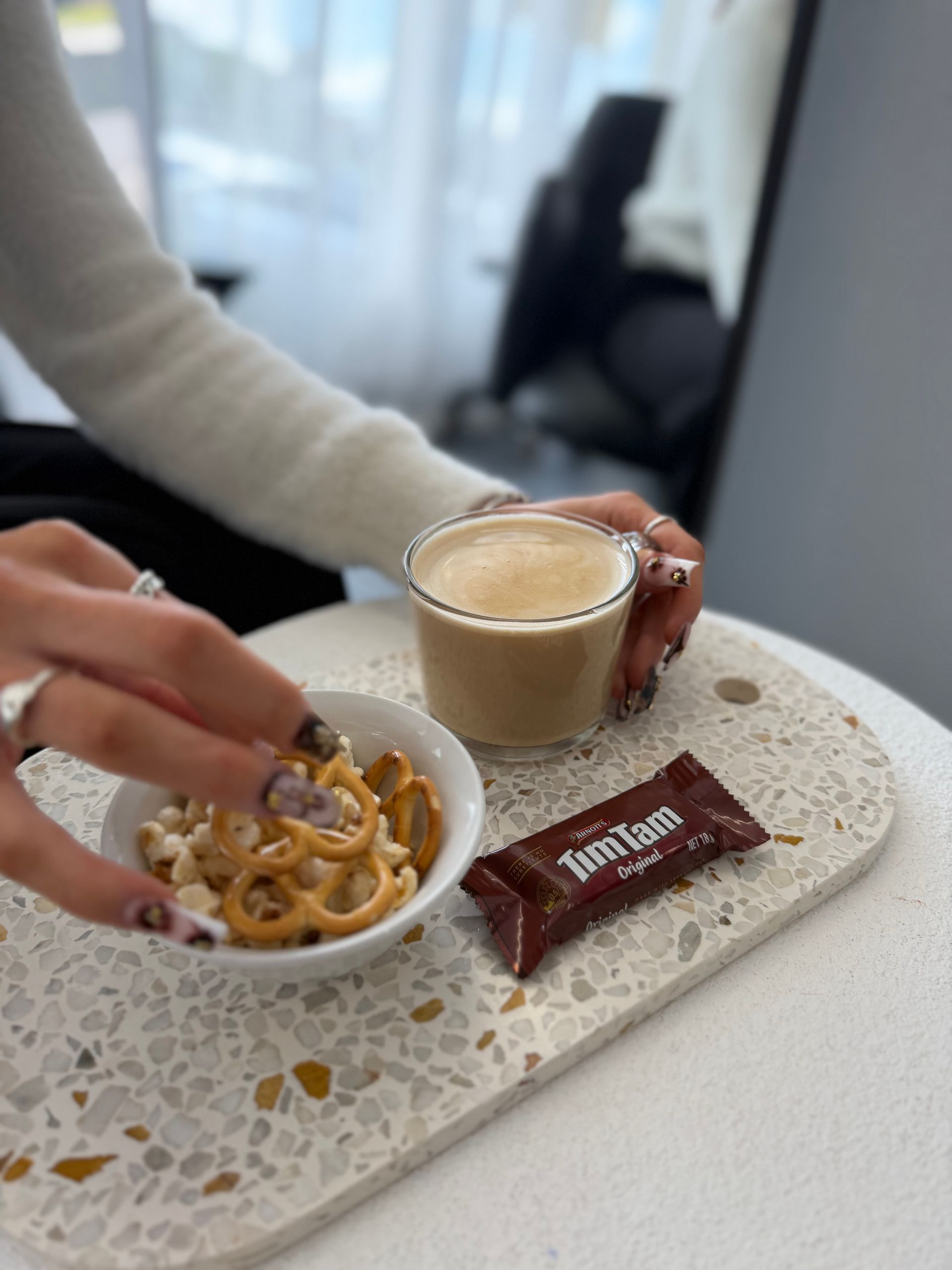 Hands holding a small breakfast tray with coffee, cereal, and a chocolate bar on a white table — Elysian Salon In Wyong, NSW