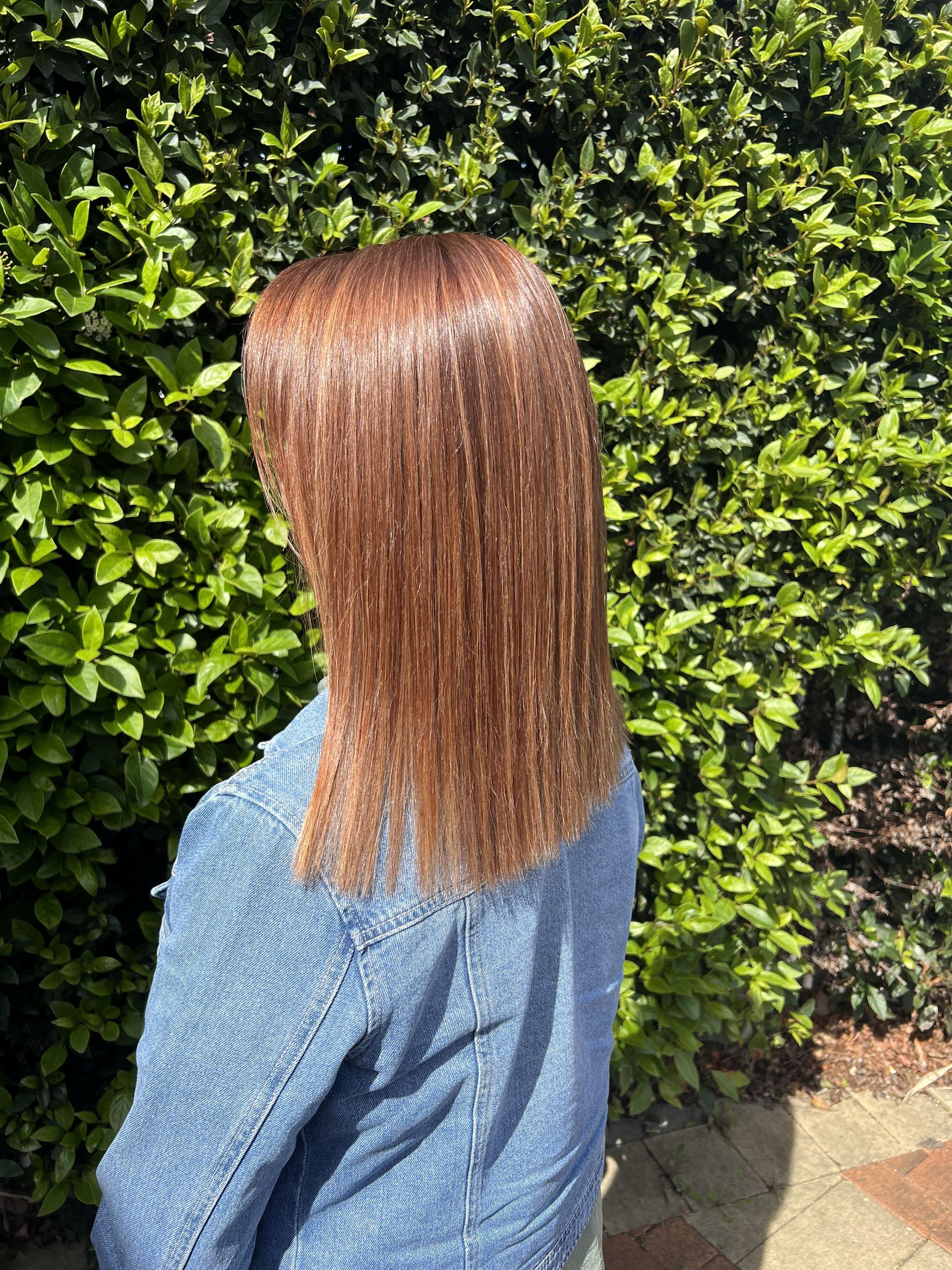 A Woman Wearing a Hat and a Bun is Standing in Front of a Plant — Elysian Salon In Wyong, NSW