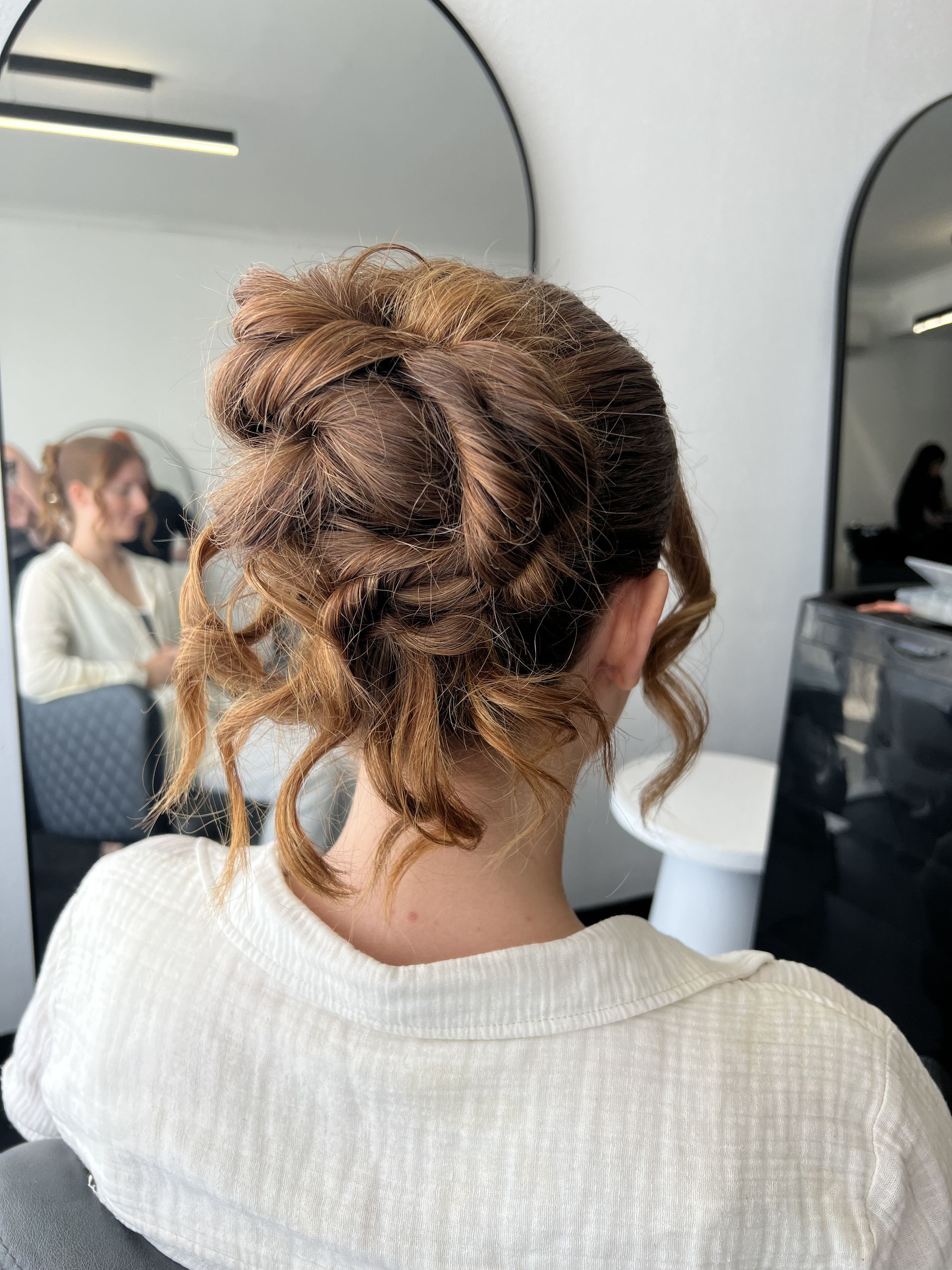 Back of a person with curly hair pinned up, wearing a white top in a salon mirror area   — Elysian Salon In Wyong, NSW