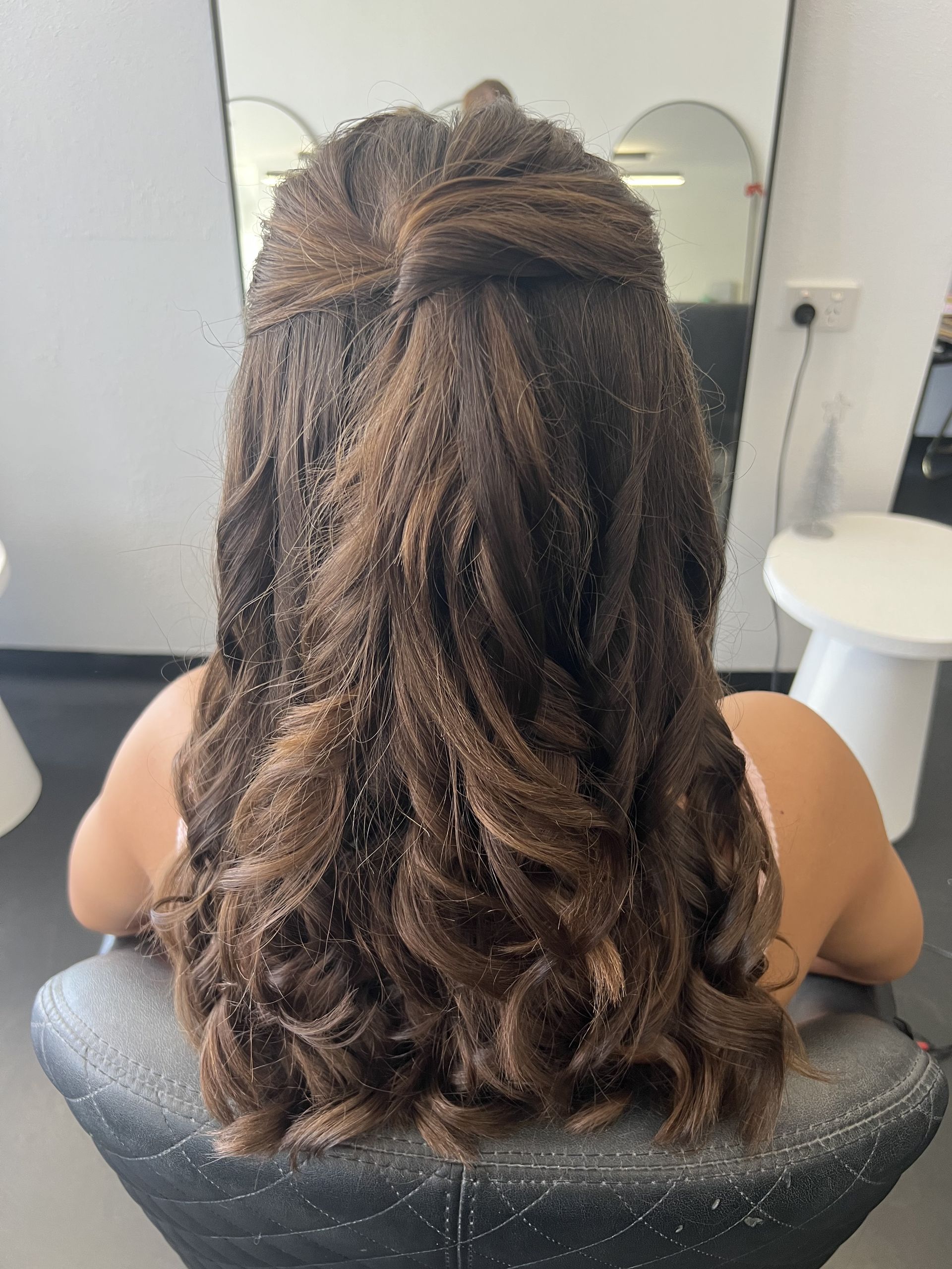 Person with wavy brown hair seated in a salon chair, viewed from behind — Elysian Salon In Wyong, NSW