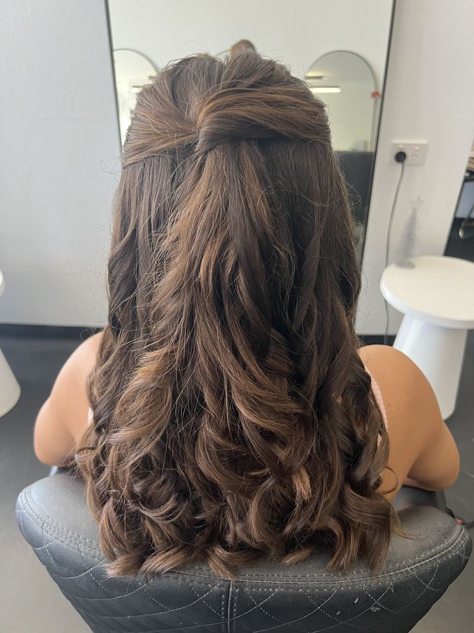 Person With Curly Blonde Hair in a Purple Top Sits in a Salon Chair — Elysian Salon In Wyong, NSW Back view of a person with long wavy brown hair in a salon chair, facing a mirror — Elysian Salon In Wyong, NSW