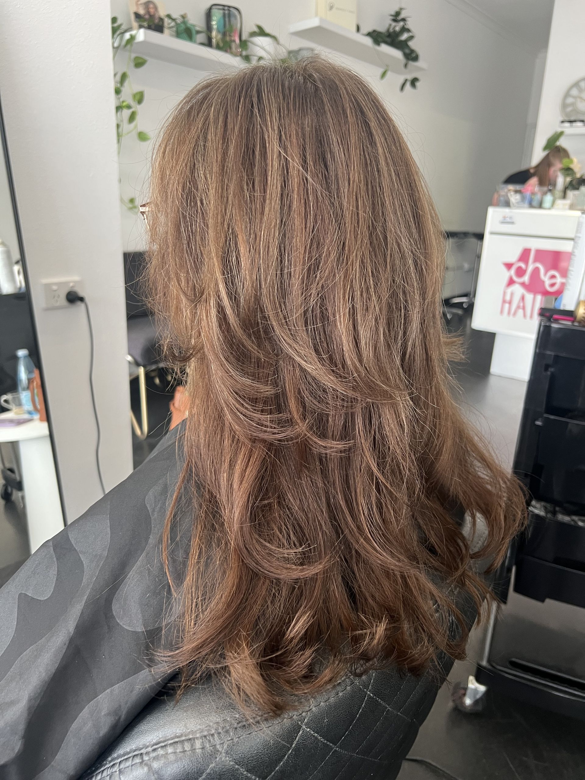 Back view of shoulder-length brown hair with blonde highlights in a salon chair — Elysian Salon In Wyong, NSW