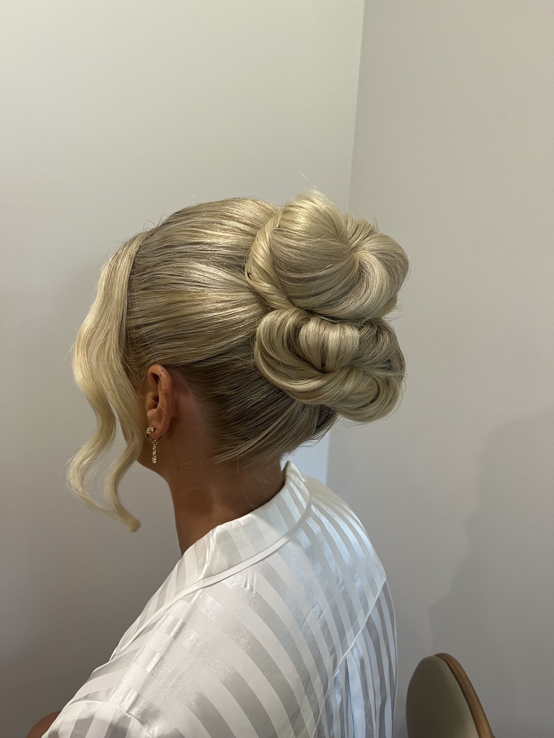 Side view of an updo hairstyle with blonde and silver braided buns against a plain wall — Elysian Salon In Wyong, NSW