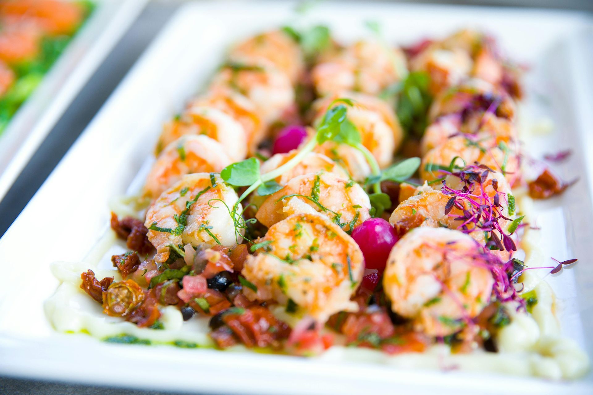 Shrimp dish with herbs, tomatoes, and purple garnishes on a white platter.