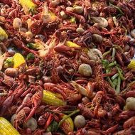 Crawfish boil: red crawfish, corn, potatoes, sausage, and vegetables in a large pile.
