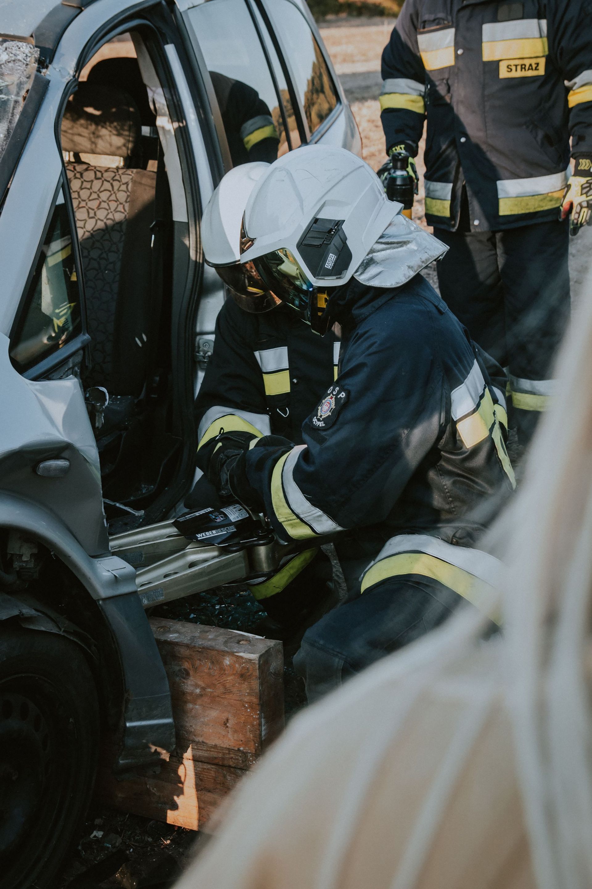 Un bombero con casco blanco rescata a una persona de un accidente de coche.