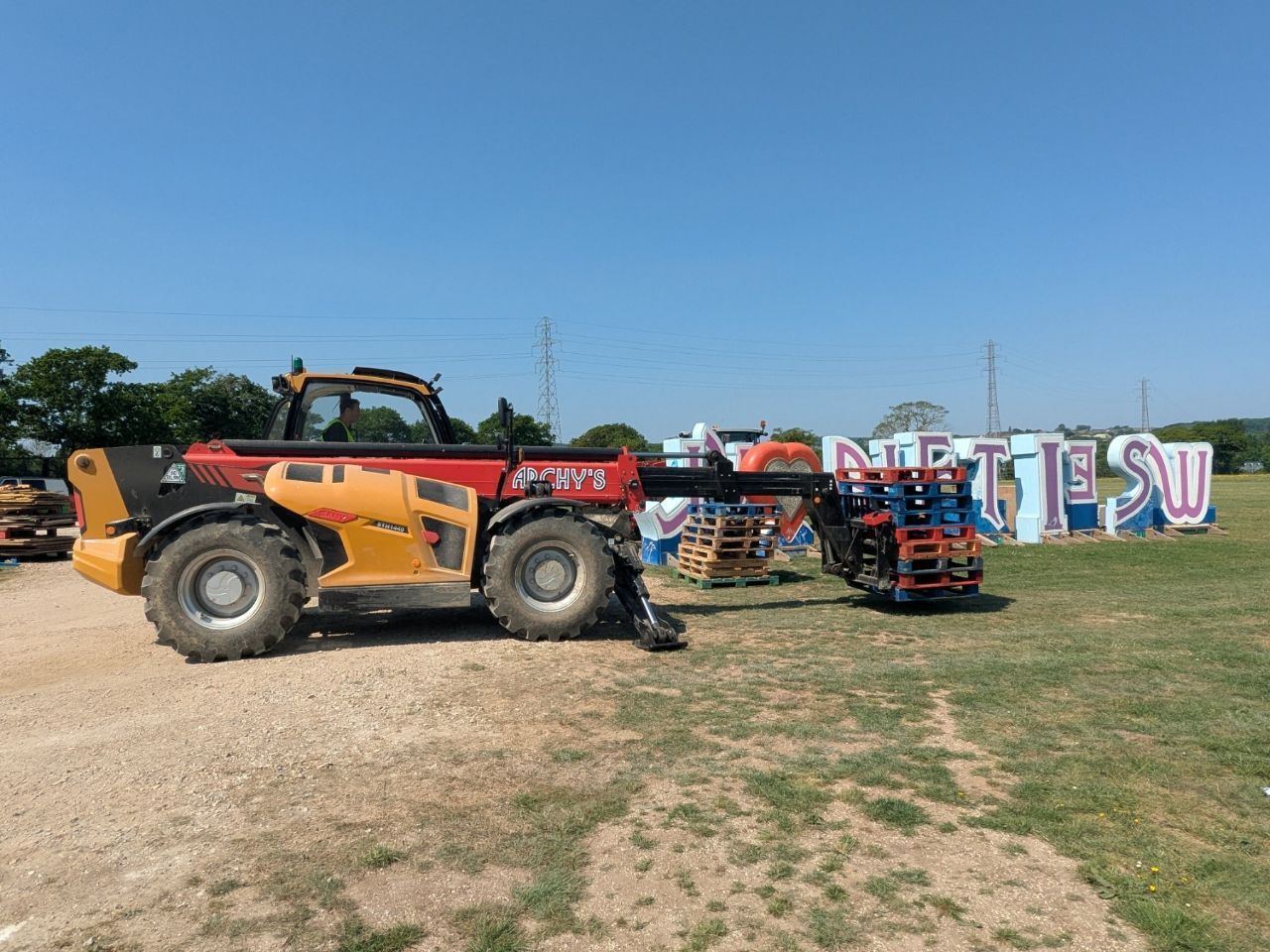 A telehandler is being used to lift a large sign in a field.