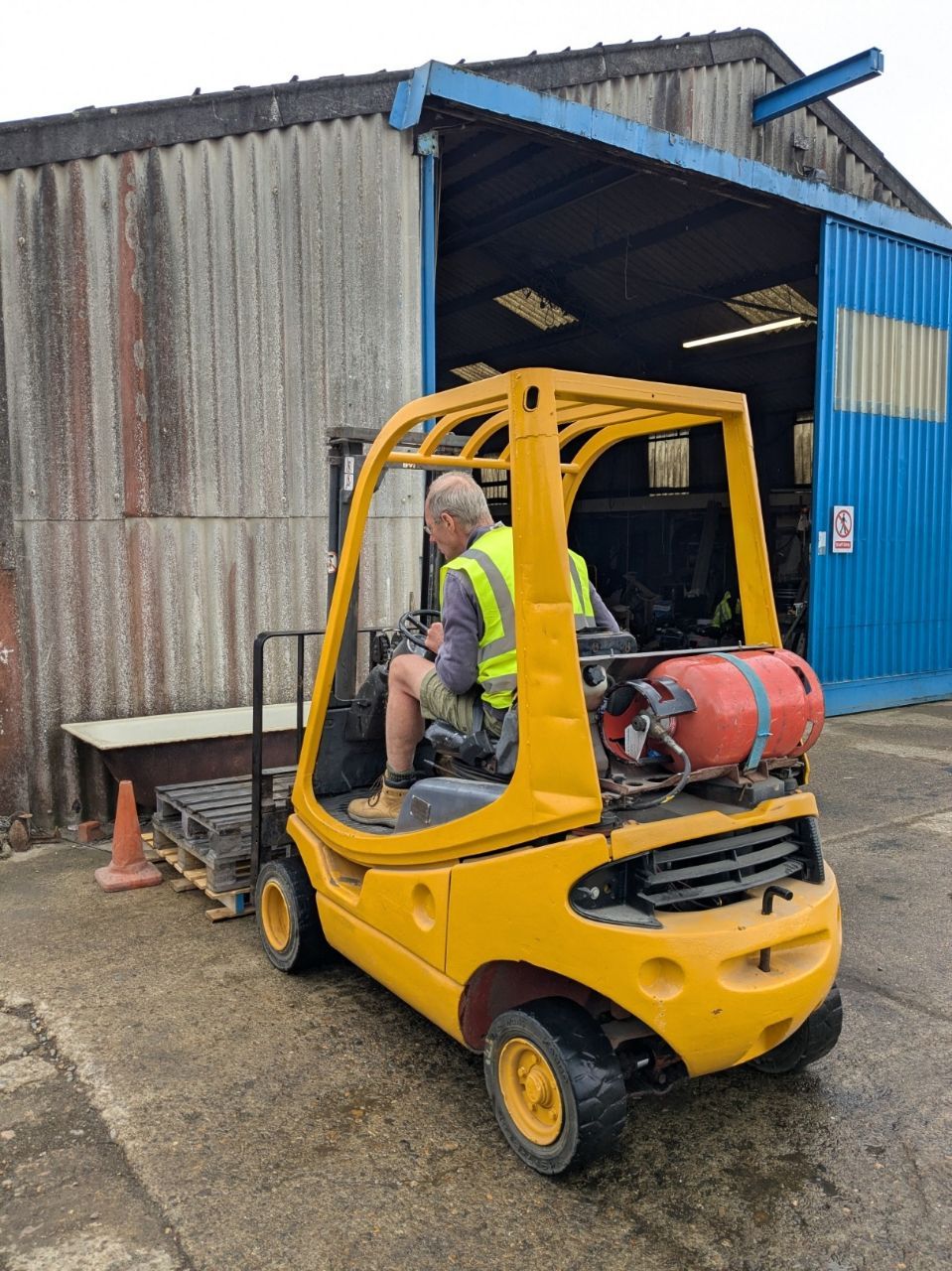 A man is driving a yellow forklift in front of a building.
