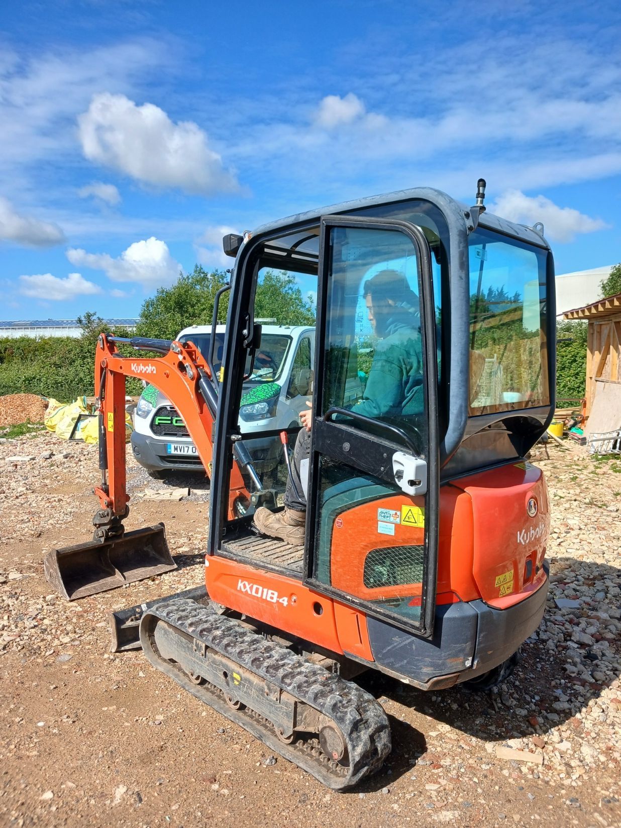 Orange mini excavator on a dirt site under a blue sky