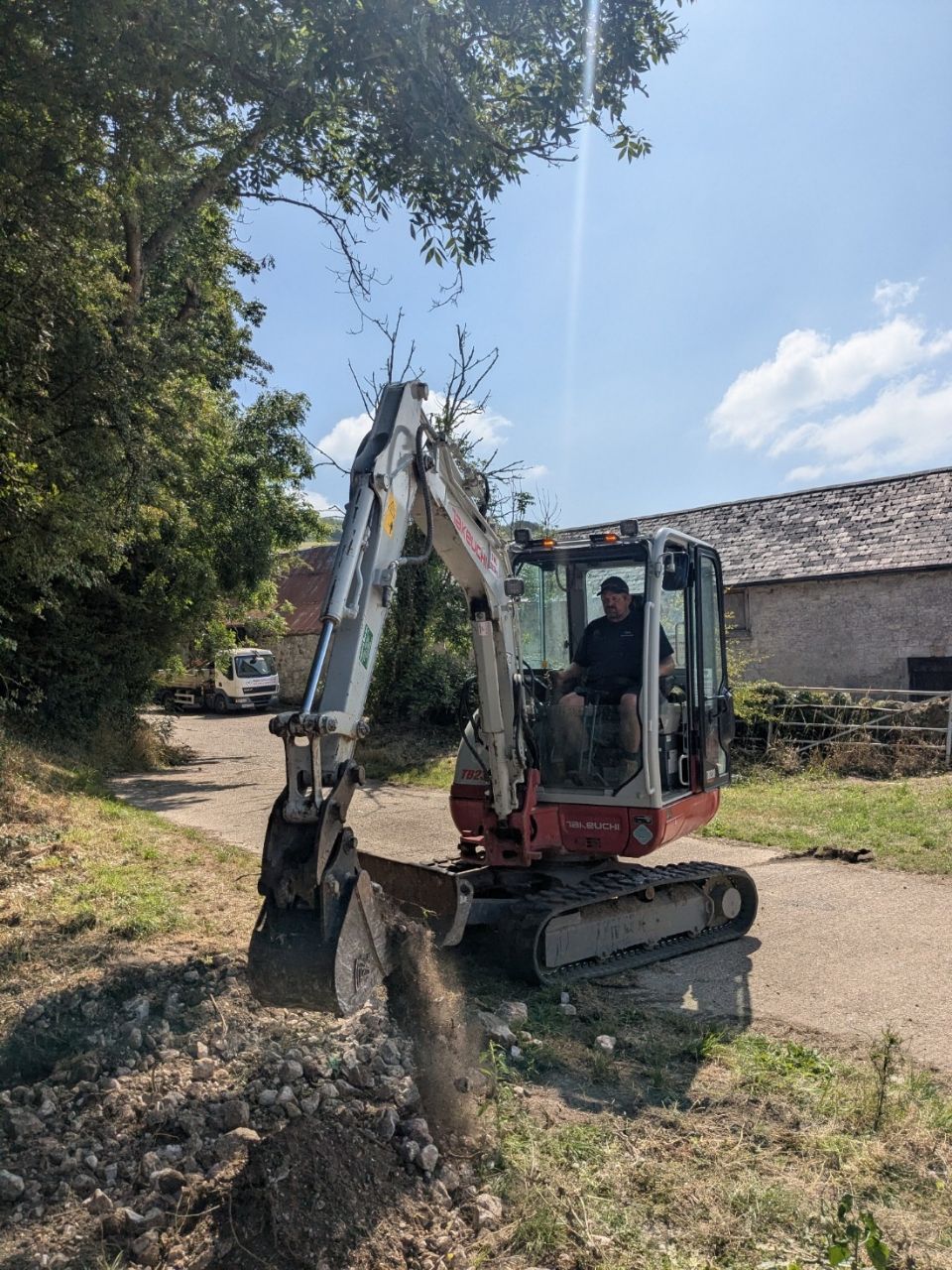 A man is driving a small excavator on a dirt road.