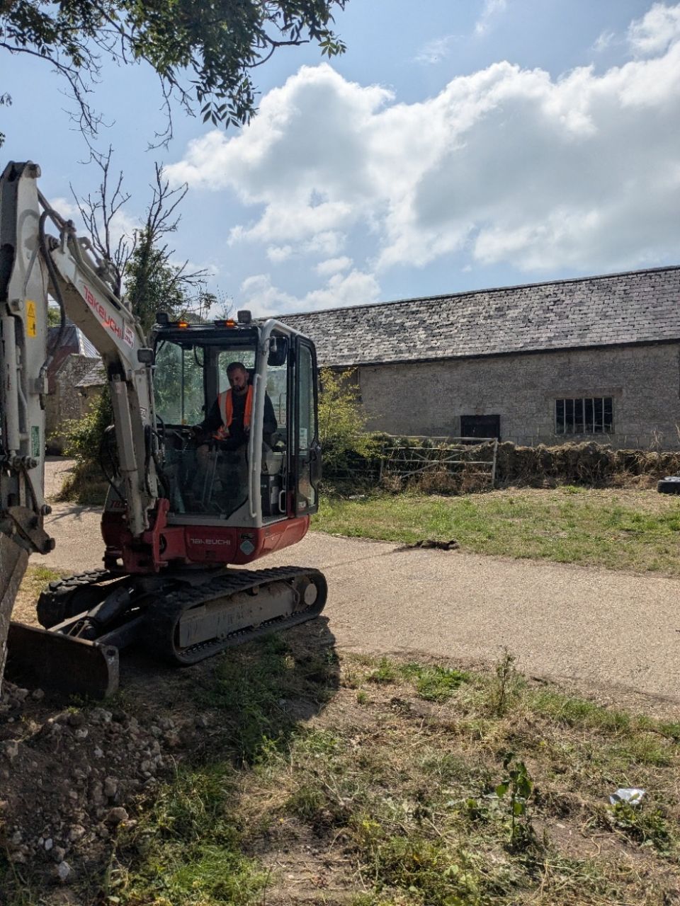 A man is driving a small excavator on a dirt road.