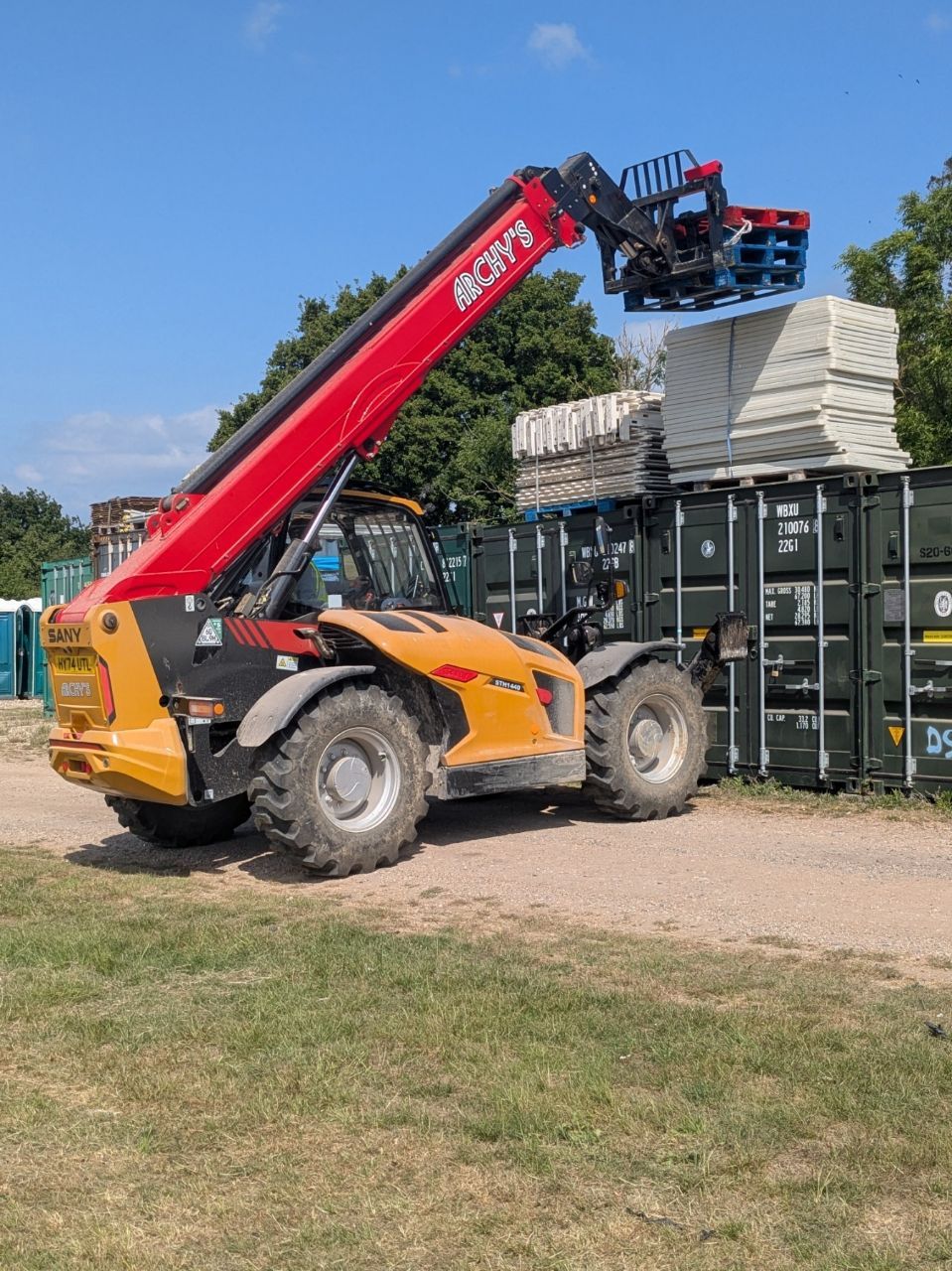 A red and yellow forklift is loading a stack of shipping containers.