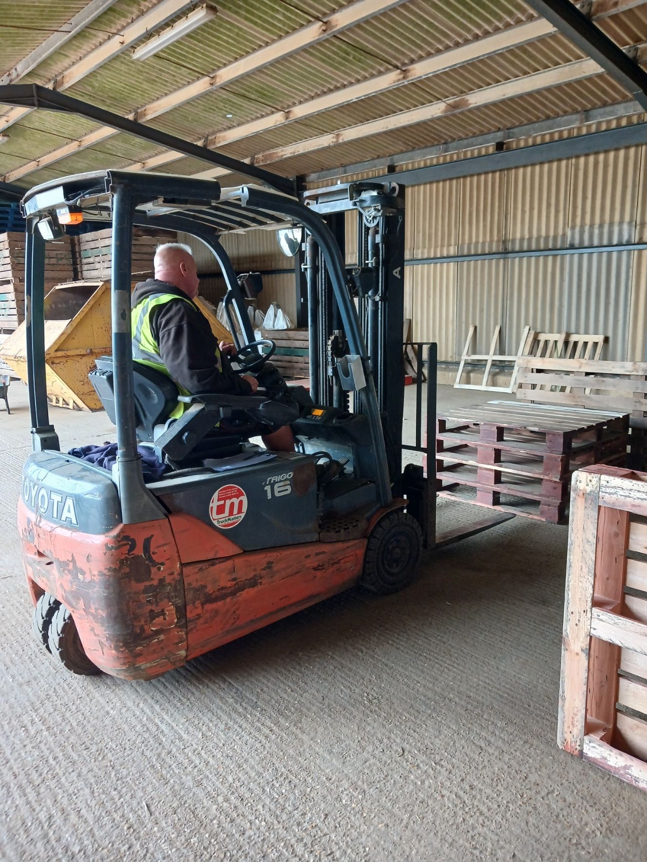 Forklift driver moving pallets inside a warehouse with wooden beams and stacked materials