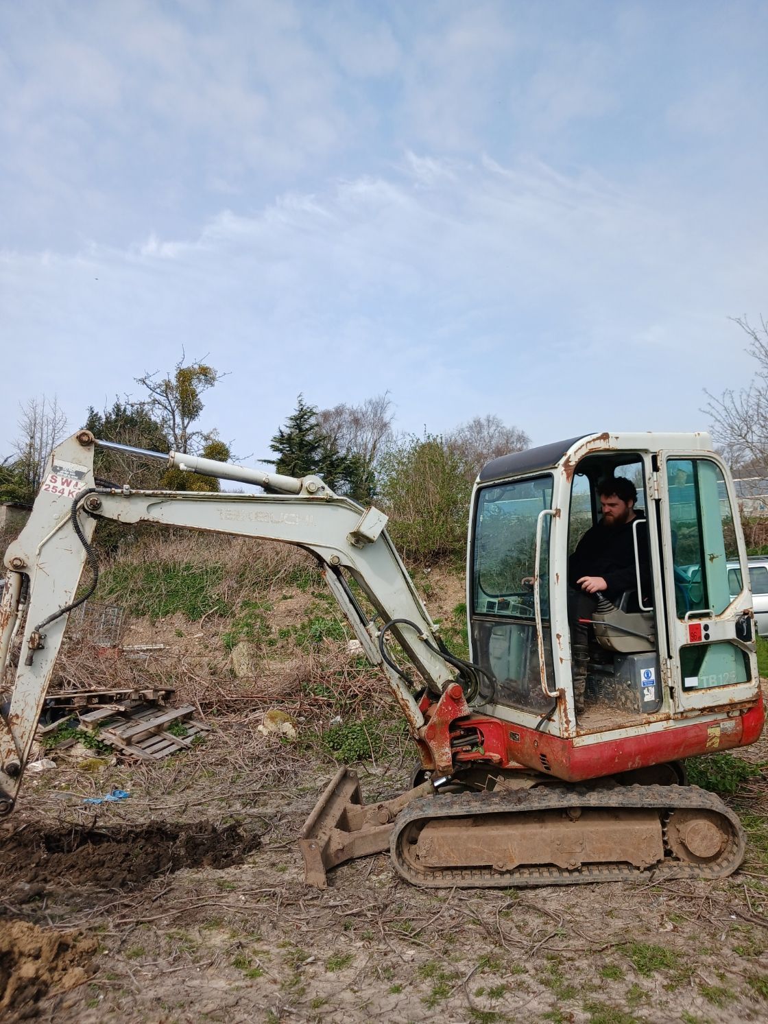 Small red excavator digging in a muddy field under a cloudy sky