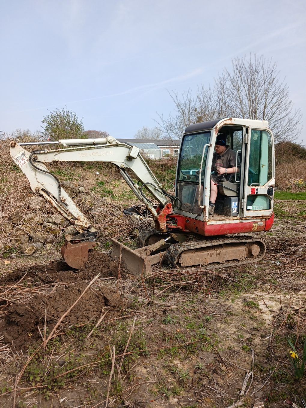 Small excavator digging dirt on a muddy hillside under a clear sky