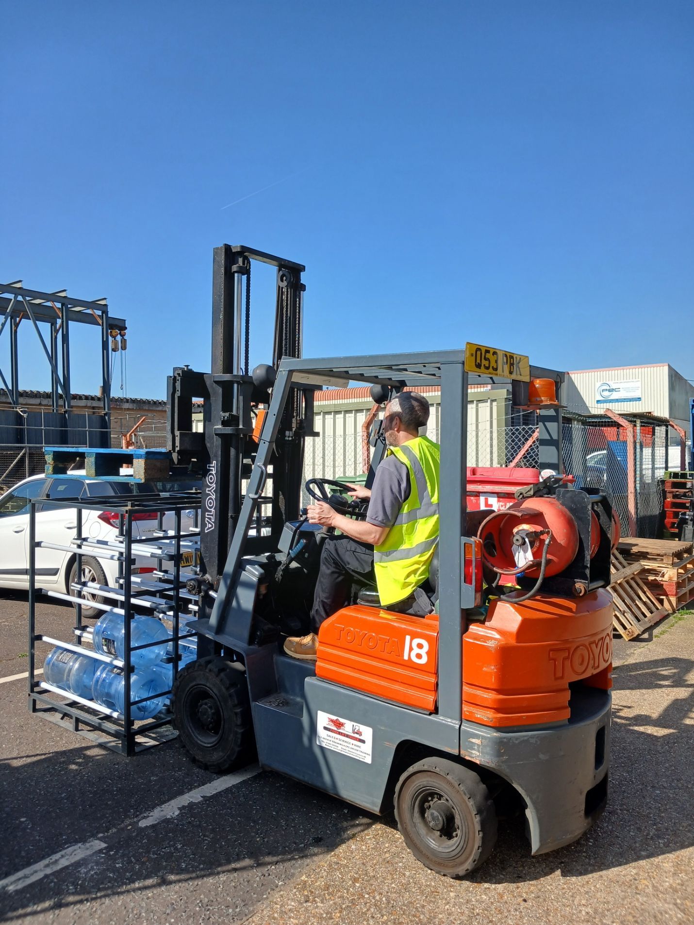 Worker driving an orange forklift beside pallets in an outdoor industrial yard