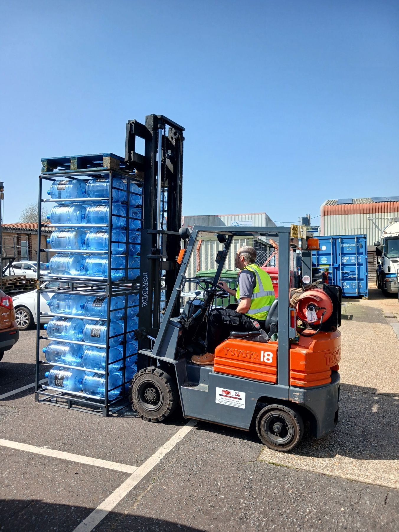 Forklift unloading stacked pallets of blue packages in an outdoor warehouse yard