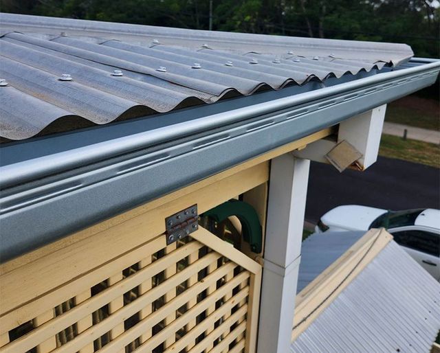 Close-up of a roof edge with gray corrugated metal roofing and white gutter above a lattice wall.