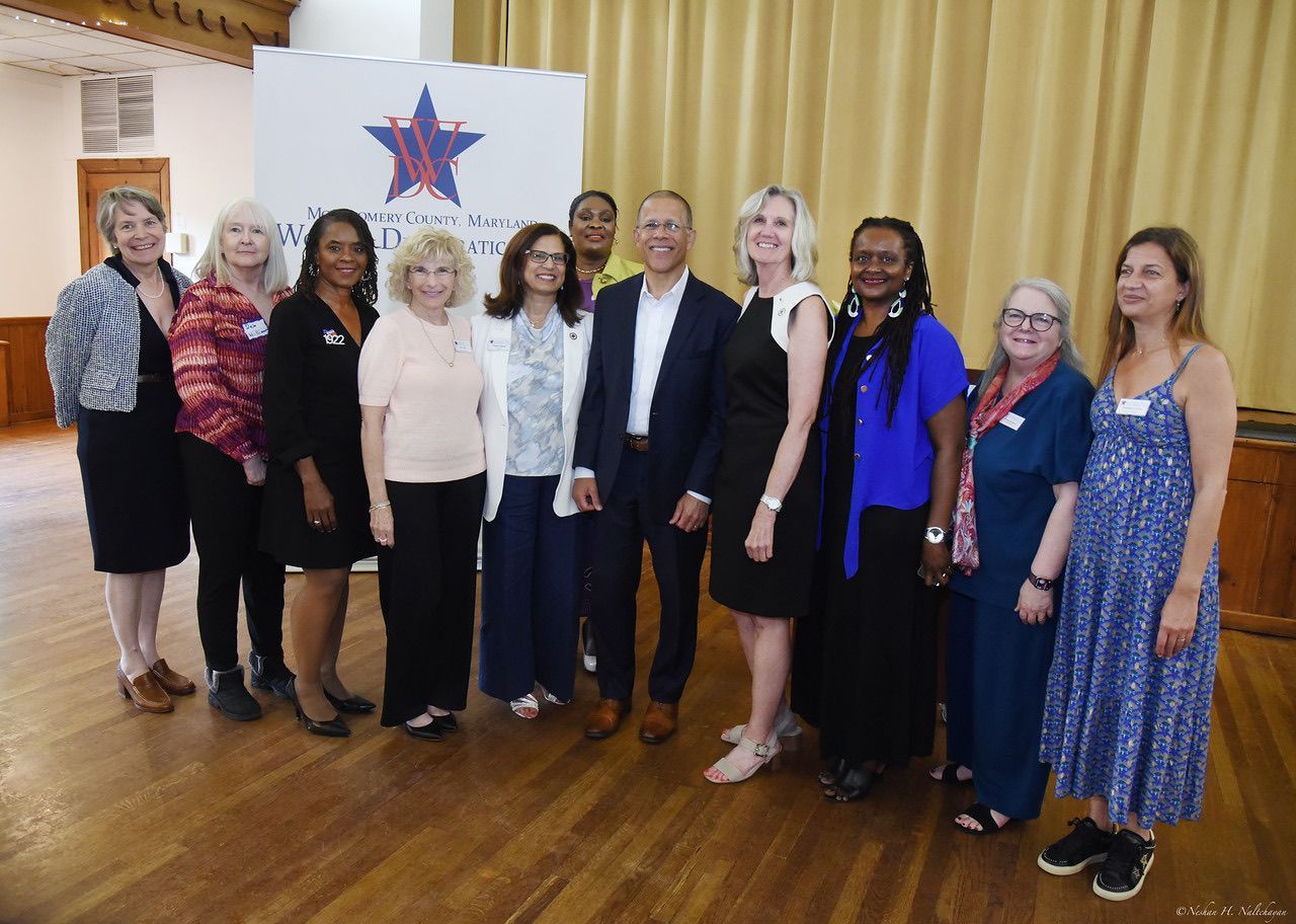 Group of people posing in front of a banner, indoors. Includes men and women smiling, in business casual attire.