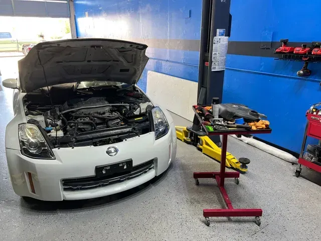 Silver car with hood open in an auto shop, beside a tool cart and a lift 