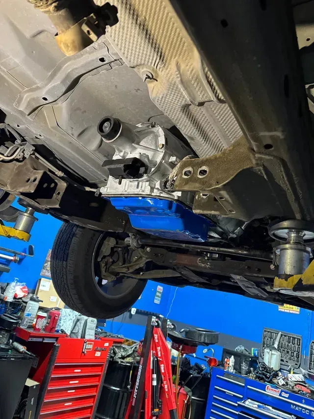 Blue classic car lifted on a shop hoist inside an auto repair garage with overhead lights | JC Auto Repair LLC
