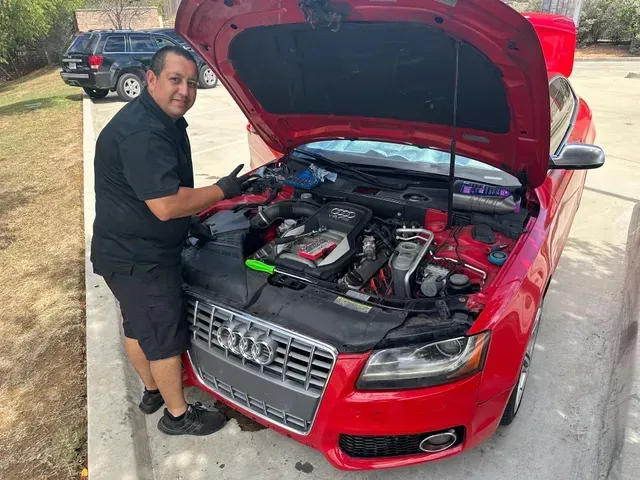 Man standing by a red car with the hood open, working on the engine in a parking lot | JC Auto Repair LLC