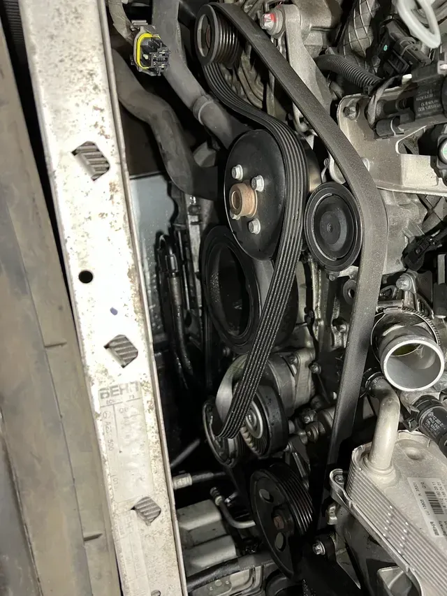 Close-up of a car engine bay with belts, pulleys, hoses, and a silver radiator support. | JC Auto Repair LLC