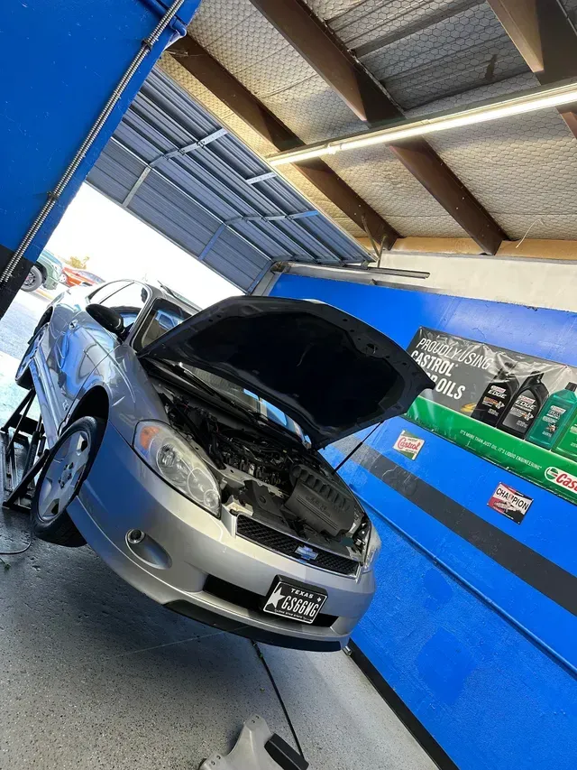Silver car in a blue garage with its hood open, showing the engine. 