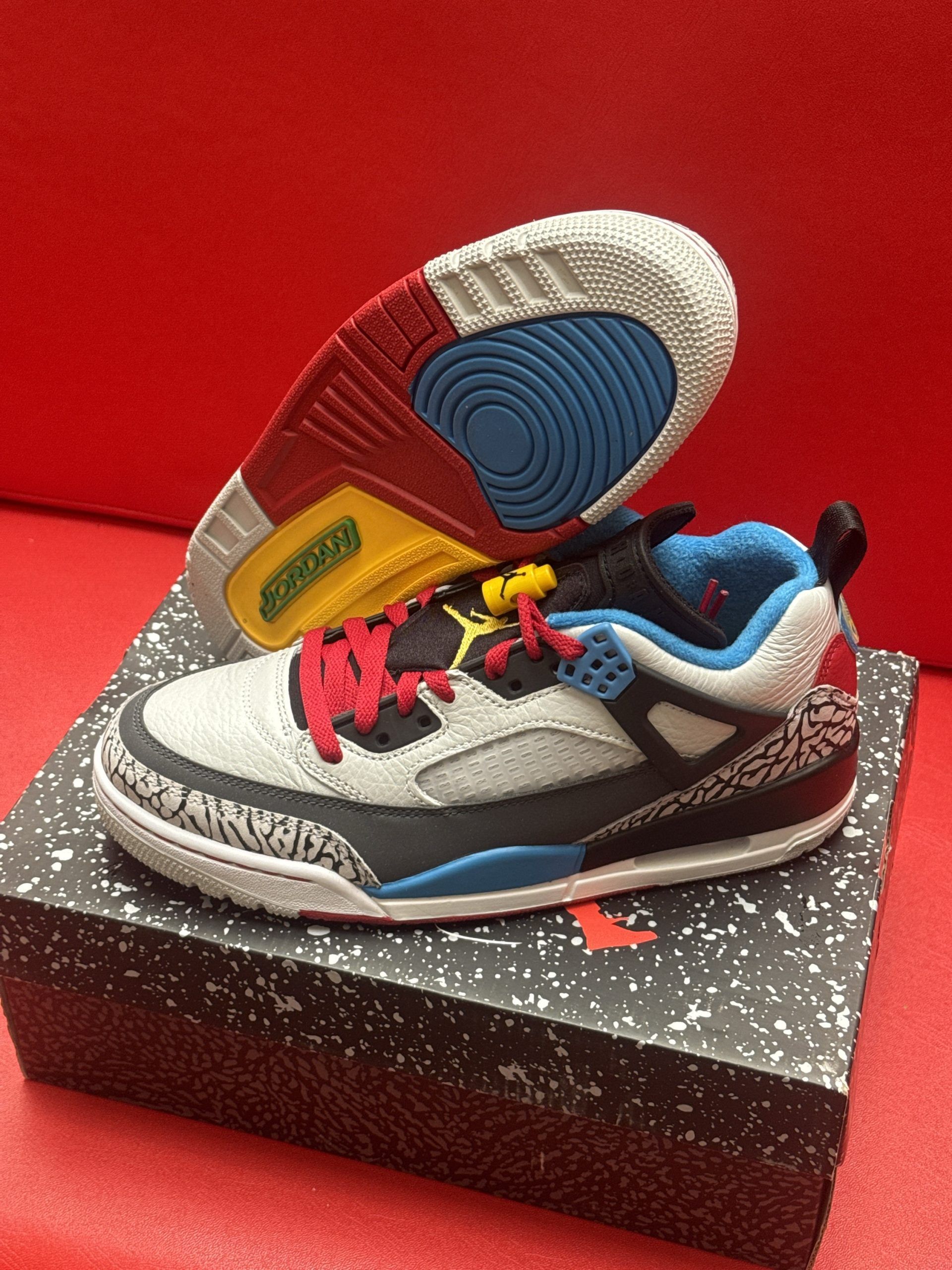 Pair of multi-colored Jordan sneakers on a shoebox against a red backdrop, showing sole detail.