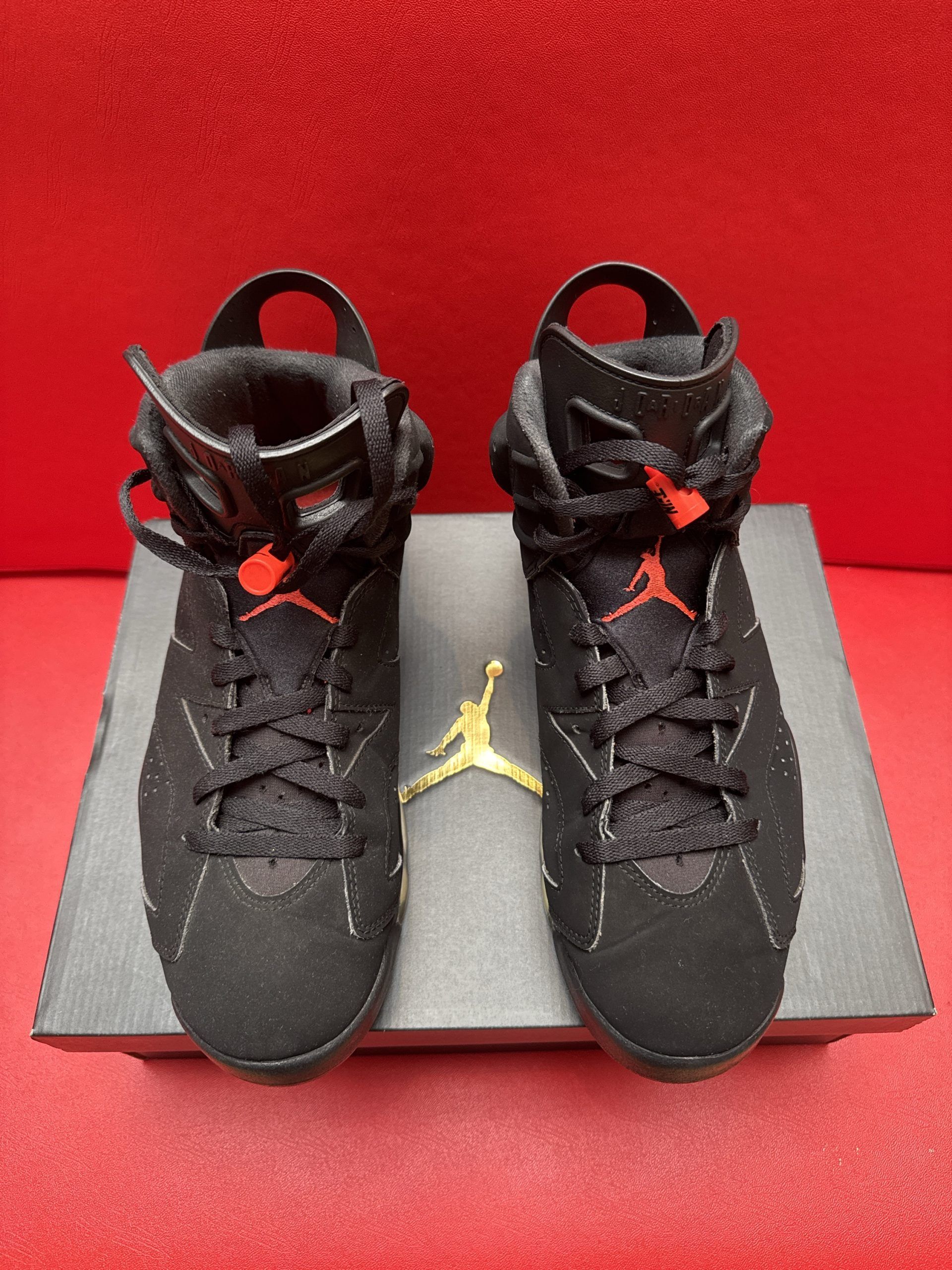 Black and red Air Jordan 6 sneakers on a box, with one turned to show the sole on a red surface.