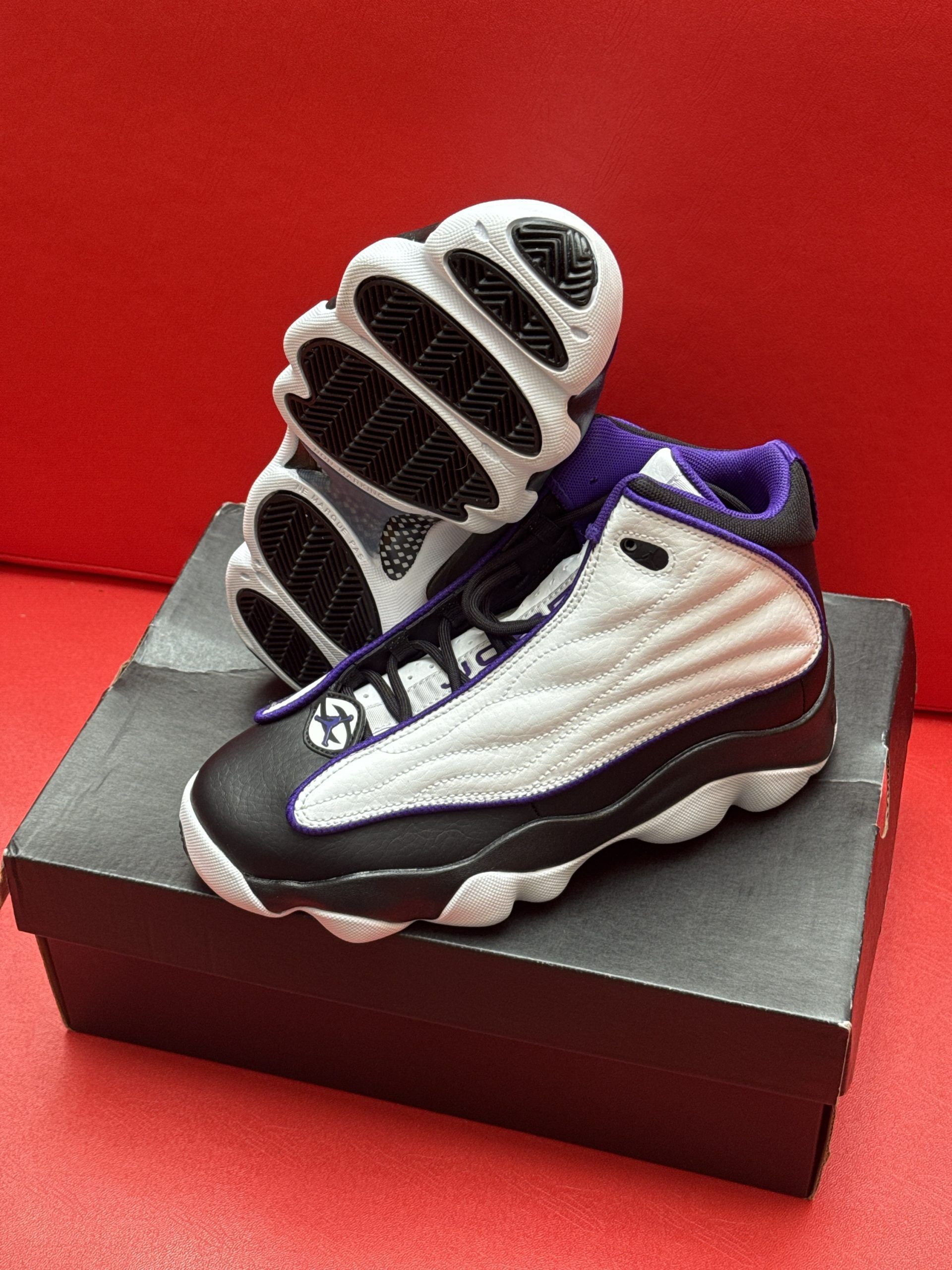 Infant Air Jordan sneakers on a shoebox. White, black, and purple color scheme against a red background.