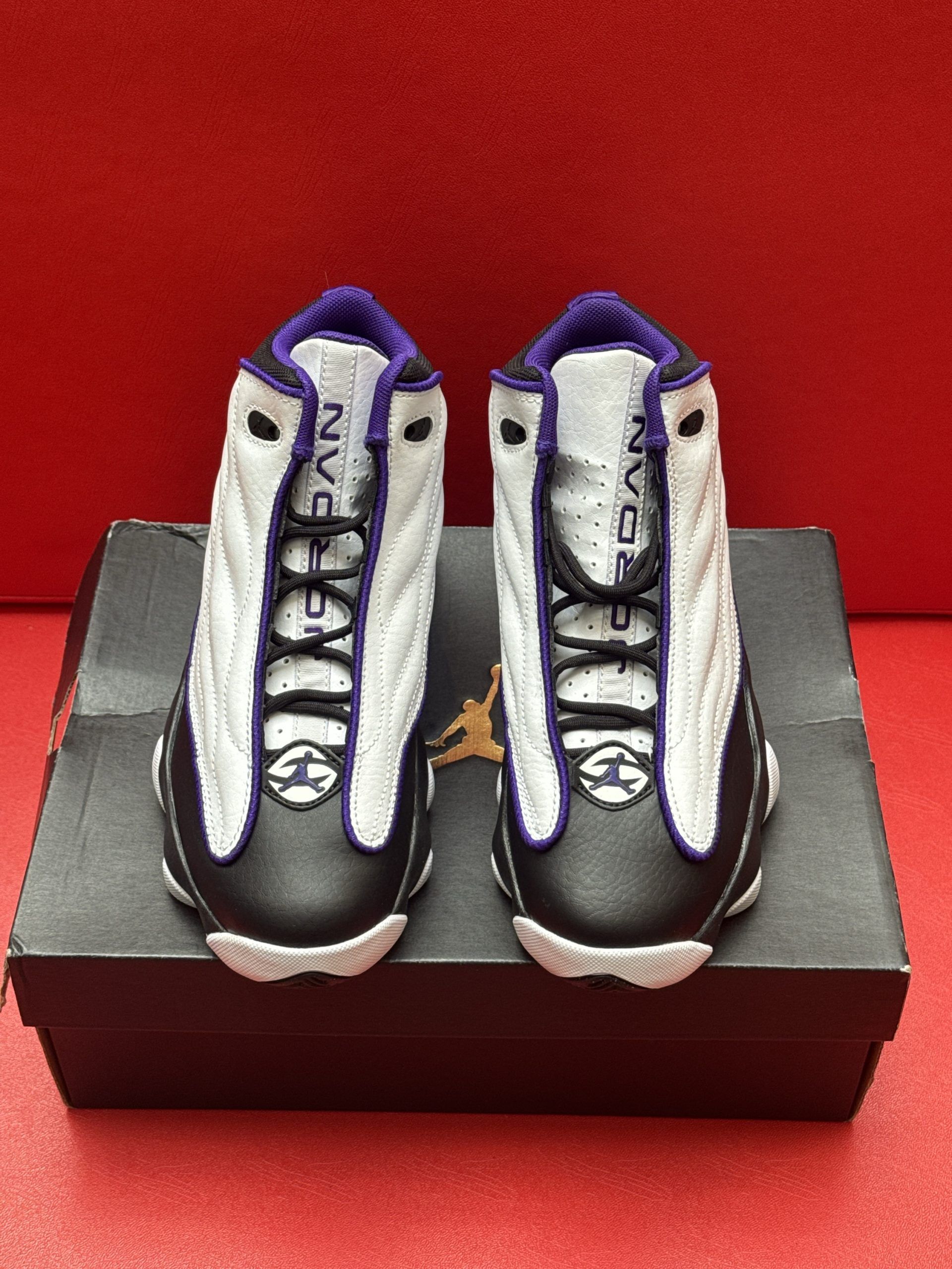 Infant Air Jordan sneakers on a shoebox. White, black, and purple color scheme against a red background.