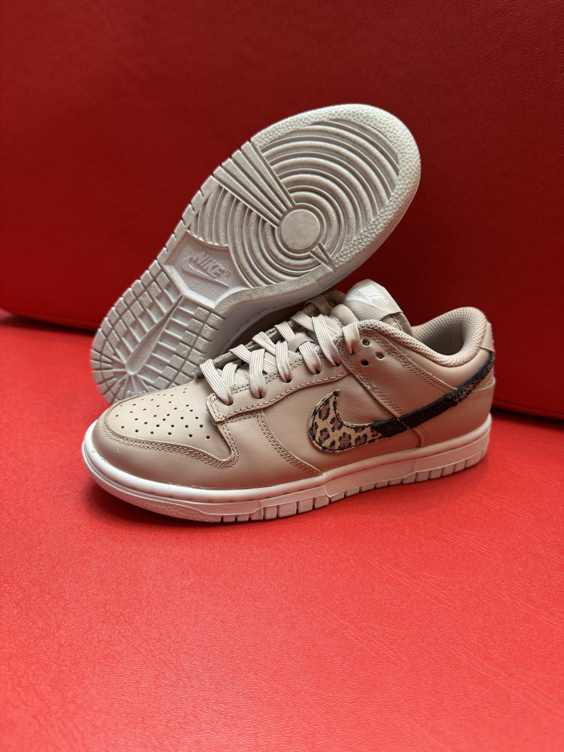Tan and black Nike Dunk low sneaker with animal print swoosh, resting on a red surface.