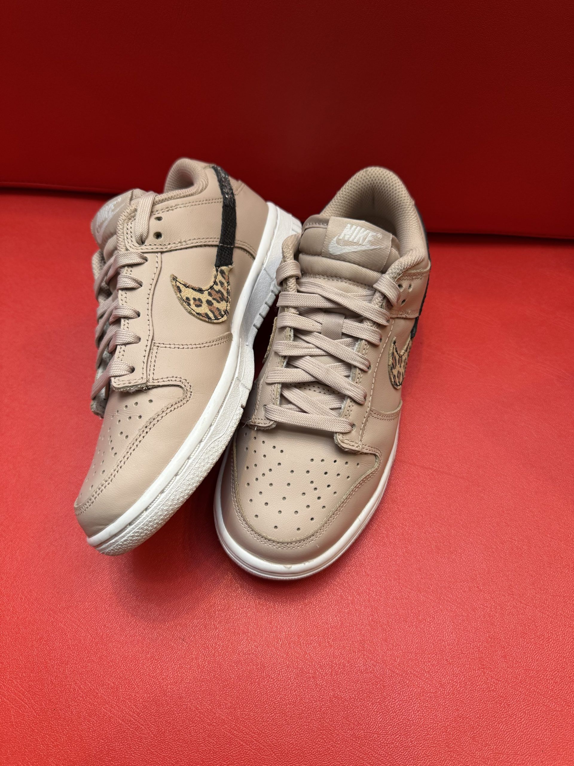 Tan and black Nike Dunk low sneaker with animal print swoosh, resting on a red surface.